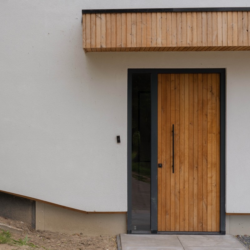Houten voordeur met zijlicht in de witte gevel van de gerenoveerde woning in Sleeuwijk
